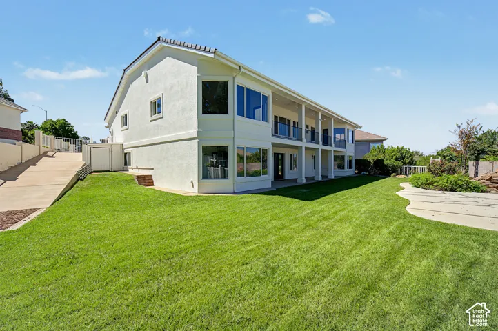 Two-story stucco exterior with multiple balconies, expansive windows, a large lawn, and a paved driveway