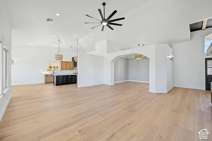Light wood-finish flooring throughout, vaulted ceilings with recessed lighting, black ceiling fan, kitchen area with dark cabinetry, arched entryway to dining area