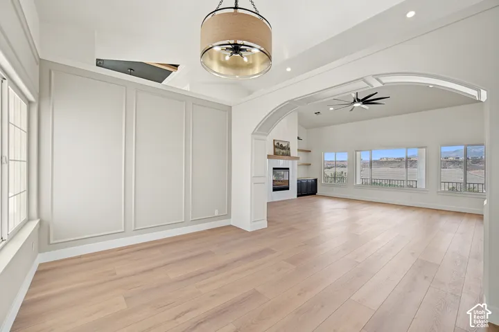 Expansive open-concept room with light wood-finish flooring, a decorative archway, a built-in fireplace with floating shelves, and multiple large windows