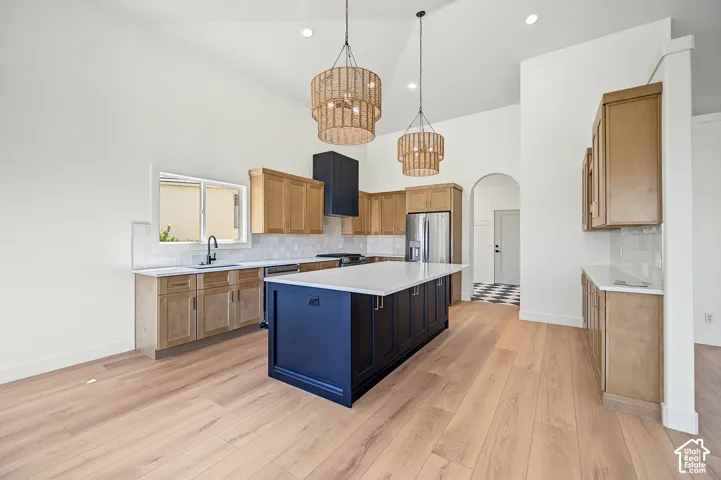 Kitchen featuring vaulted ceilings, wood-finish flooring, a central island with a solid surface countertop, wood cabinetry, and pendant lighting