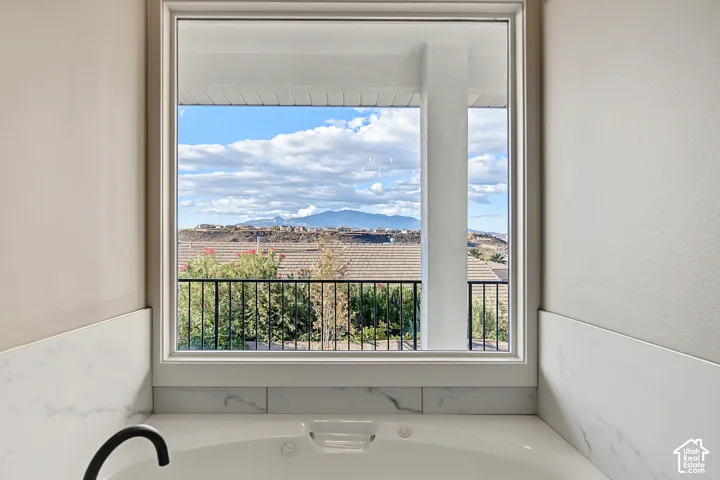 Soaking tub with white surround, large window, mountain backdrop, and black railing