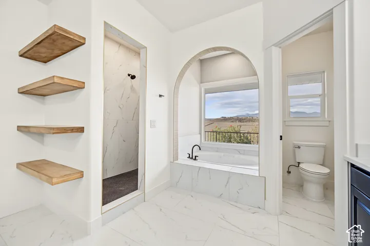 White tile flooring, built-in soaking tub with a black faucet, arched alcove, walk-in shower with tile surround, and floating wood shelves