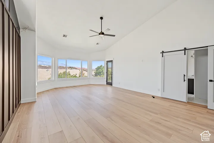 Vaulted ceilings, light wood-finish flooring, a bay window configuration, a ceiling fan, and sliding barn doors