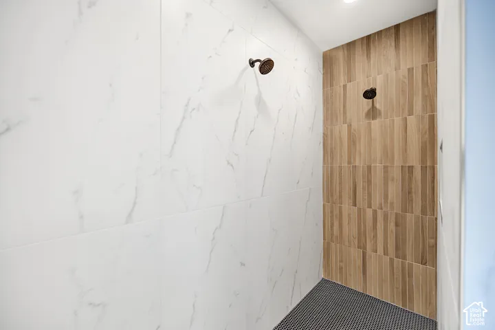 Shower stall featuring large format white tiled walls with subtle veining, wood-look plank wall tiling, a dark penny tile floor, and two dark-finished shower heads