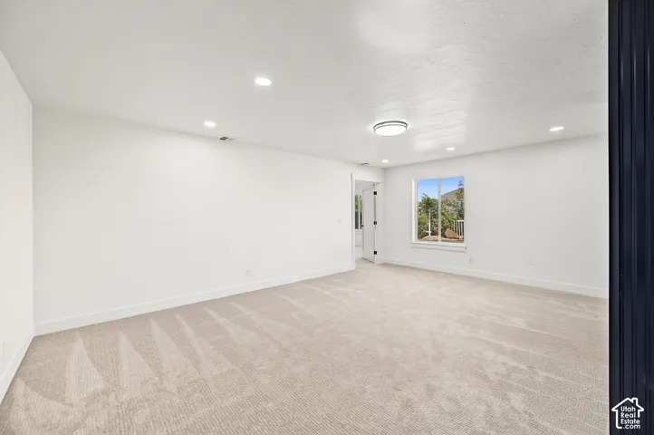 Spacious room featuring neutral carpeting, recessed lighting, a modern ceiling fixture, and a window offering natural illumination