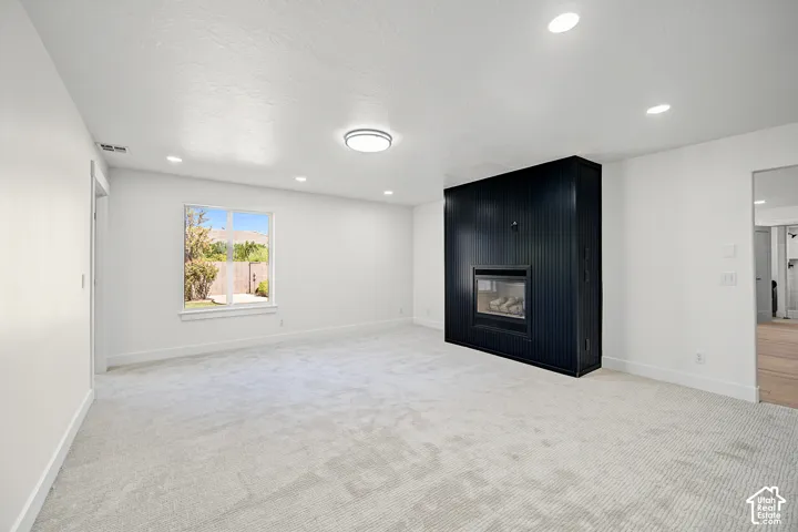 Recessed lighting, contemporary flush-mount ceiling fixture, white walls, black panel-accented fireplace, and light-toned carpeting