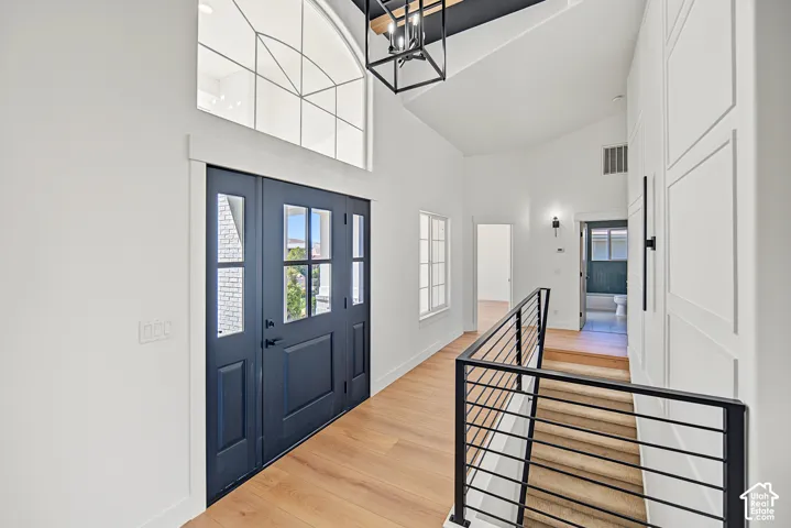 Double entry doors with glass panels, wood-finish flooring, soaring vaulted ceiling, and modern black railing