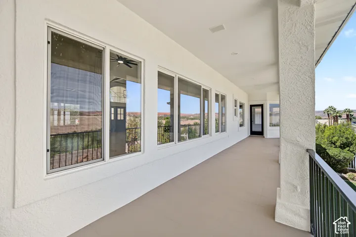 Expansive covered balcony featuring a textured stucco exterior, multiple large windows, recessed lighting, and a black wrought iron railing