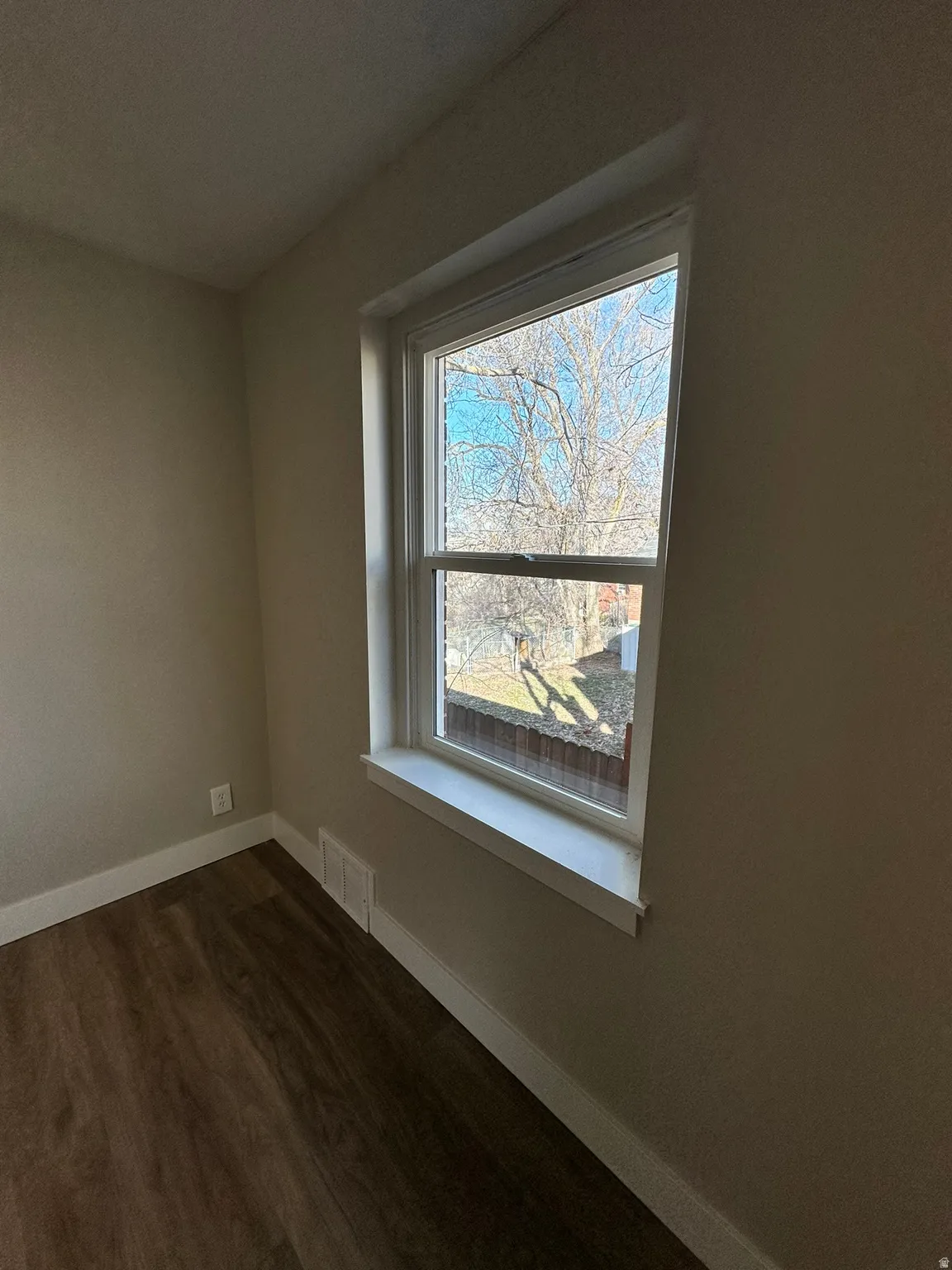 Wood-finish flooring with white trim, a double-hung window, and neutral wall paint