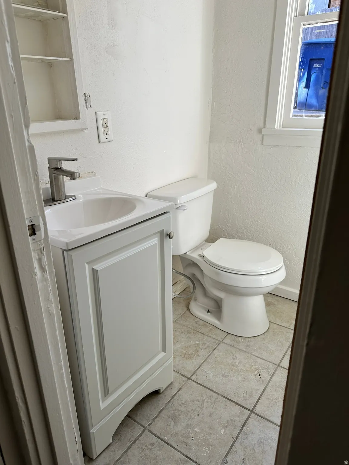 White vanity with an integrated sink and chrome faucet, white toilet, and tiled flooring