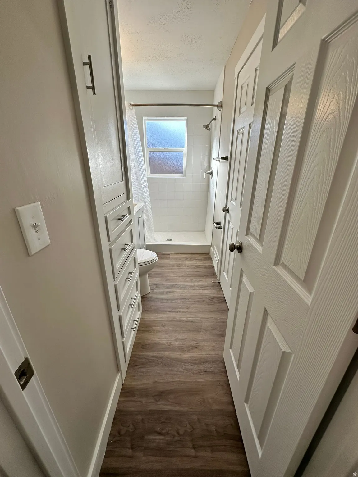 Wood-finish flooring, built-in cabinetry with drawer storage, white paneled doors, and a tiled shower with a window