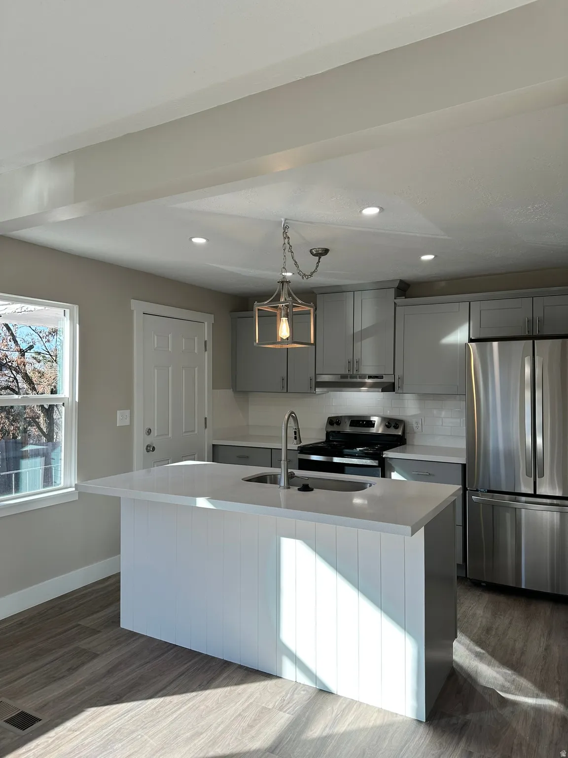Kitchen featuring wood-finish flooring, recessed lighting, a kitchen island with sink, stainless steel appliances, and gray cabinetry