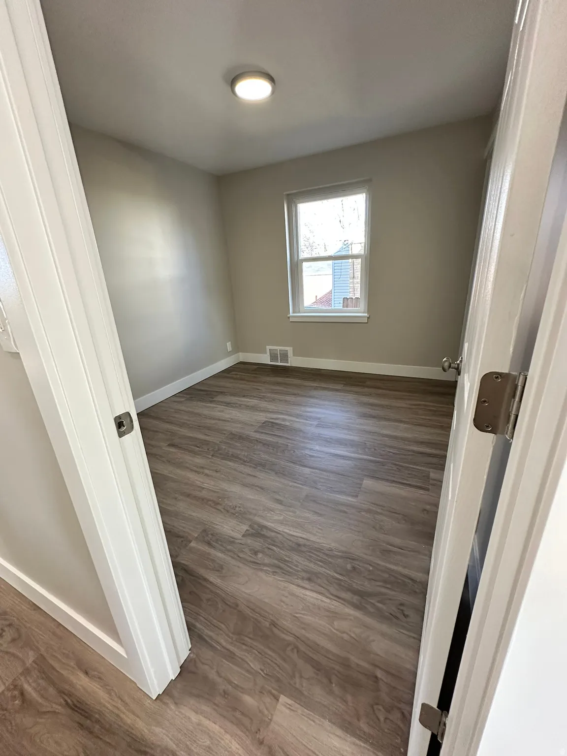 Neutral tone wall paint, wood-finish flooring, single window, and a ceiling-mounted light fixture