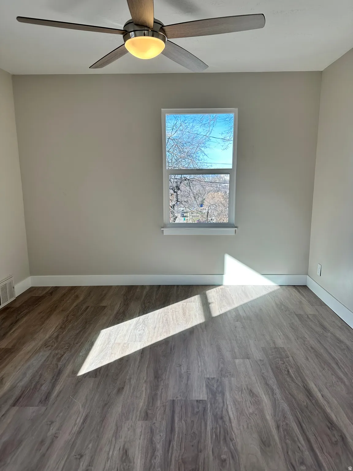 Wood-finish flooring, white trim, single window, and a ceiling fan with integrated lighting