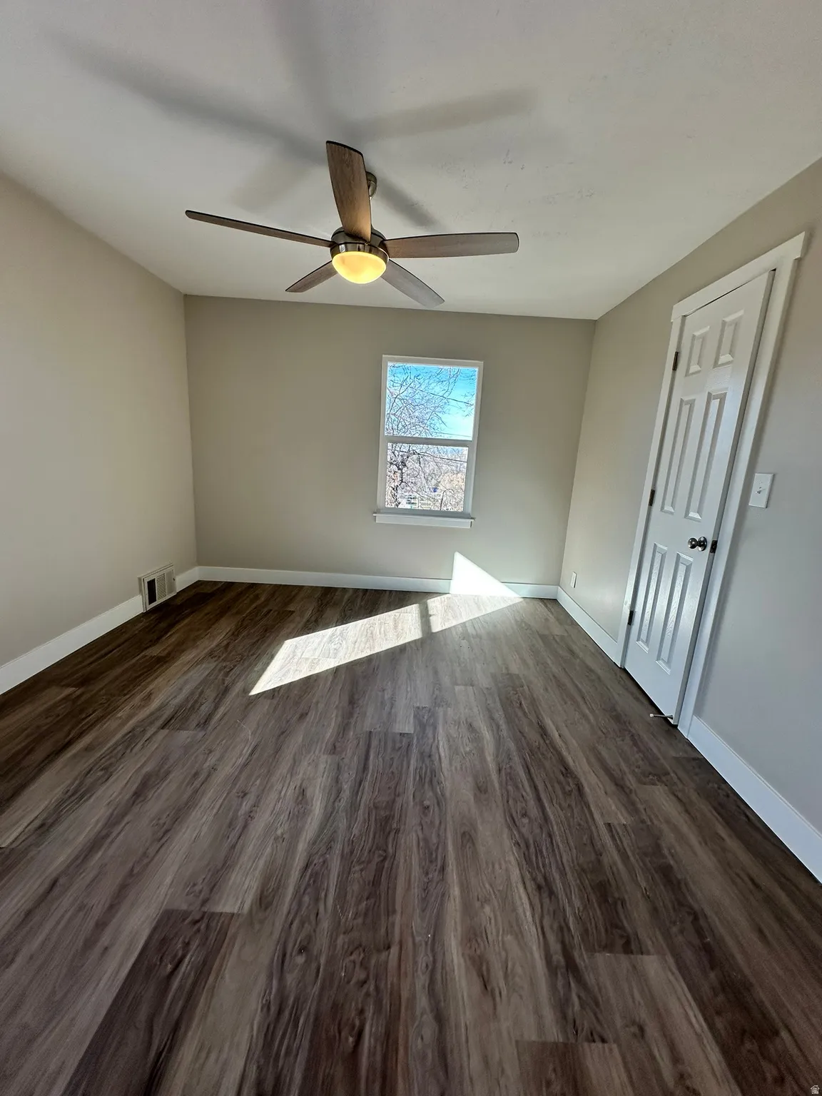 Wood-finish flooring throughout, neutral wall paint, white trim, and a ceiling fan with integrated lighting