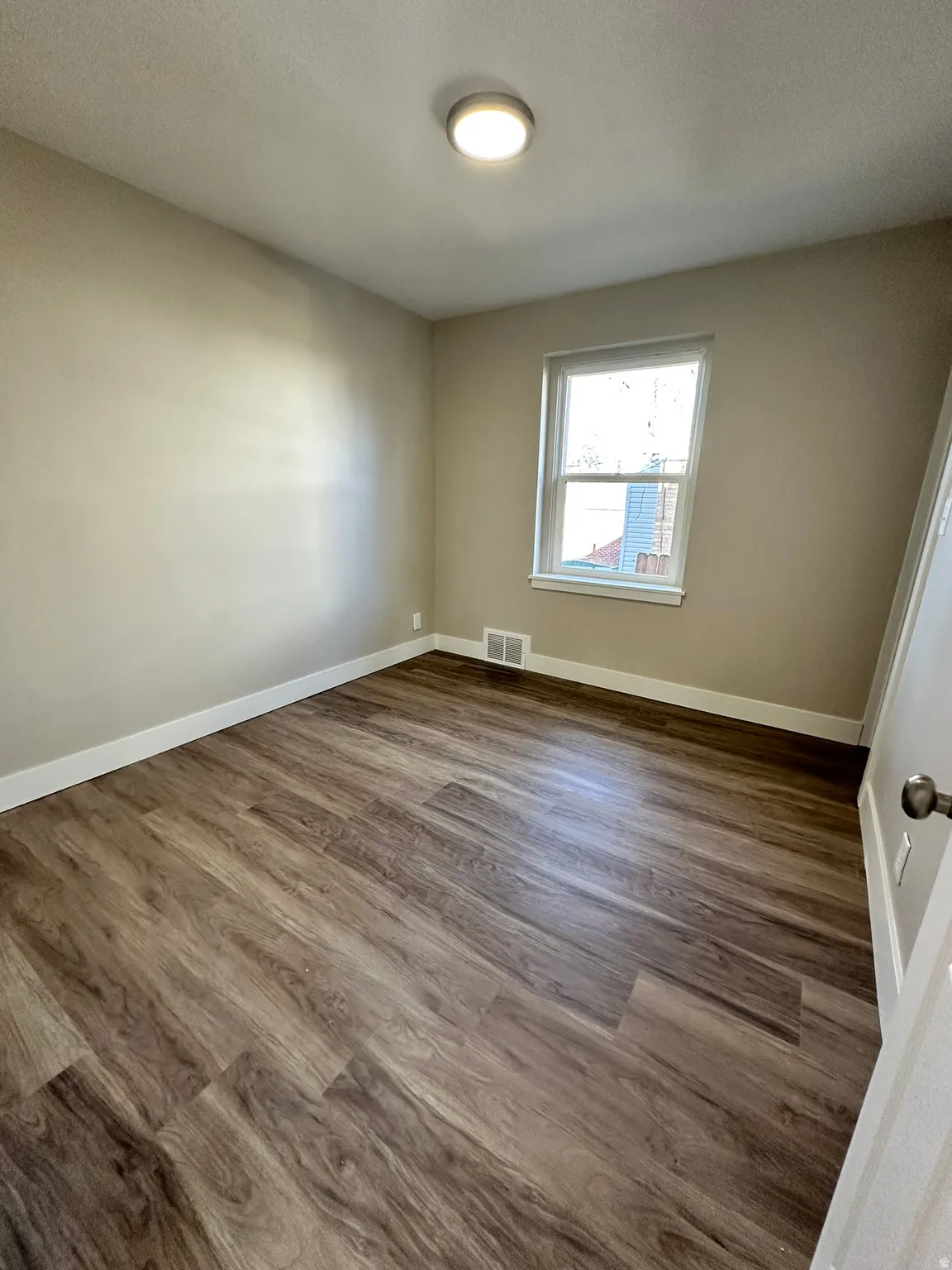 Wood-finish flooring, white trim, single window, and a flush-mount ceiling light