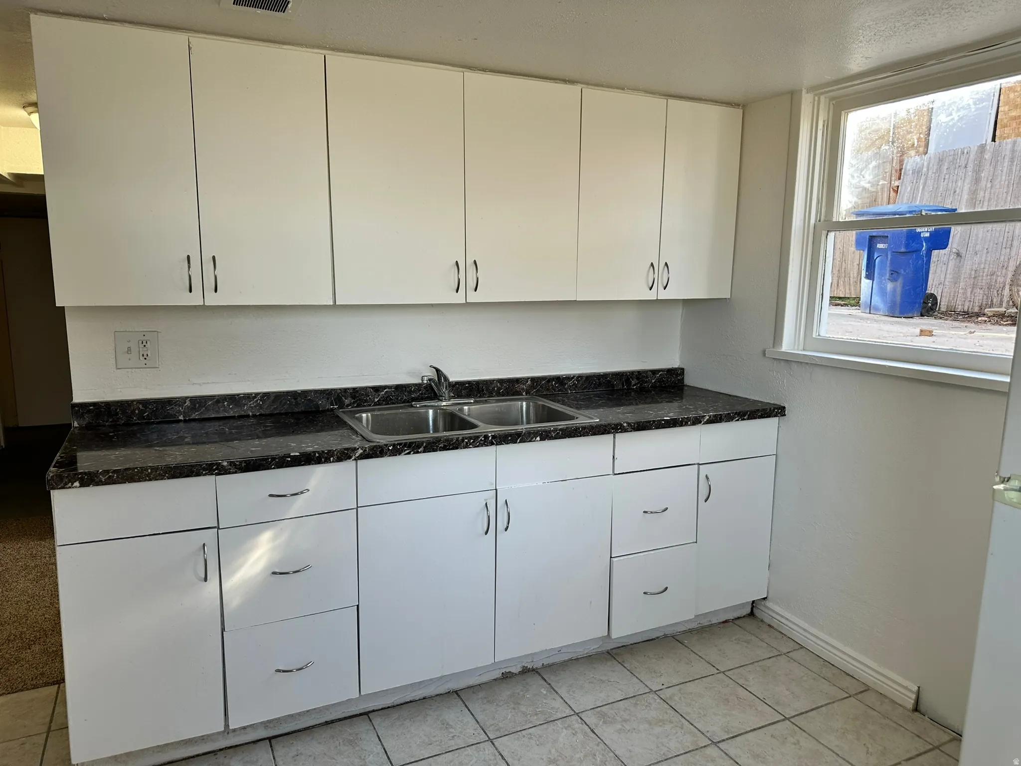 White cabinetry with brushed nickel hardware, dark speckled countertops, and a double basin stainless steel sink