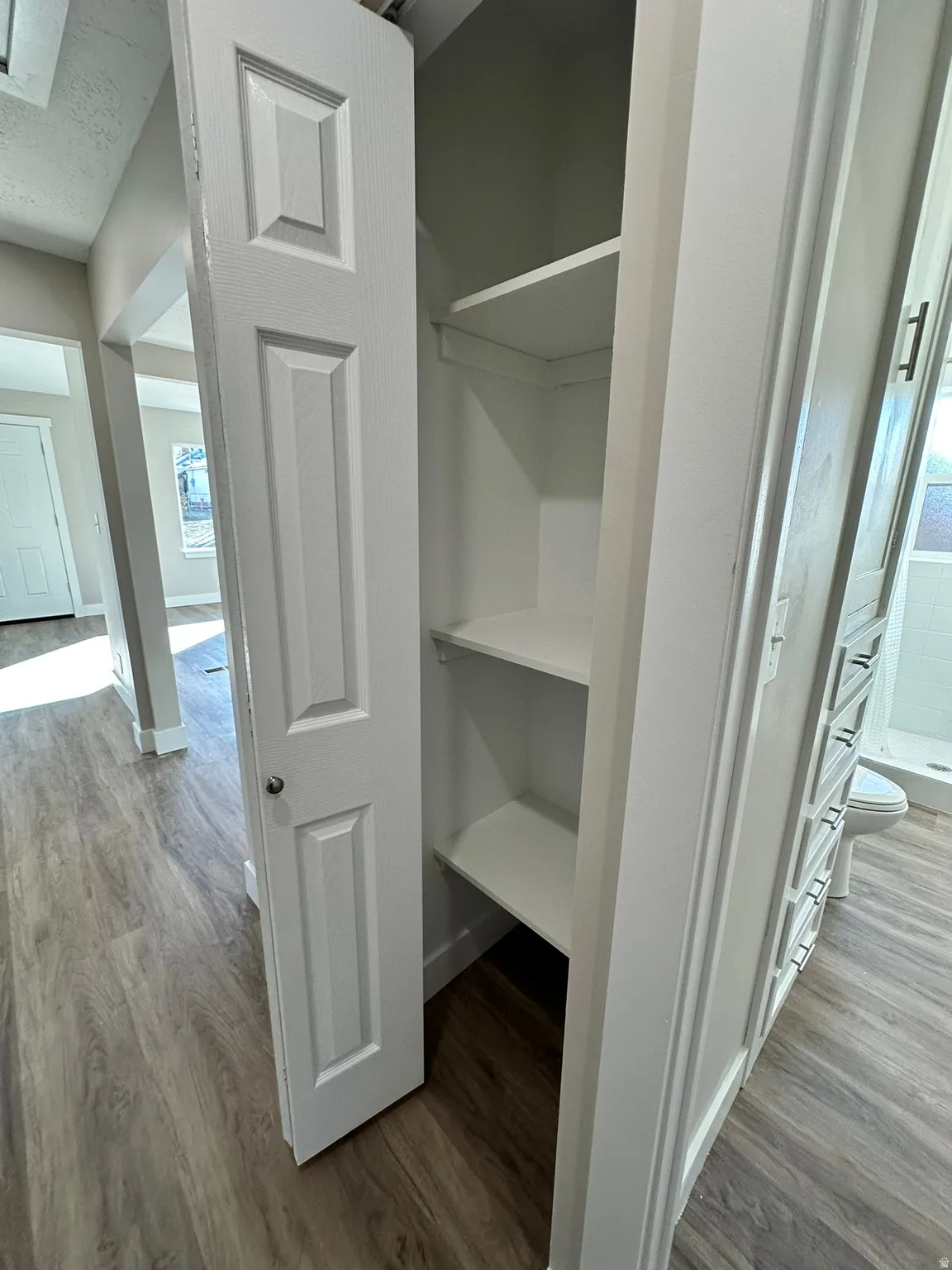 Built-in shelving with bifold door, wood-finish flooring, and crisp white trim