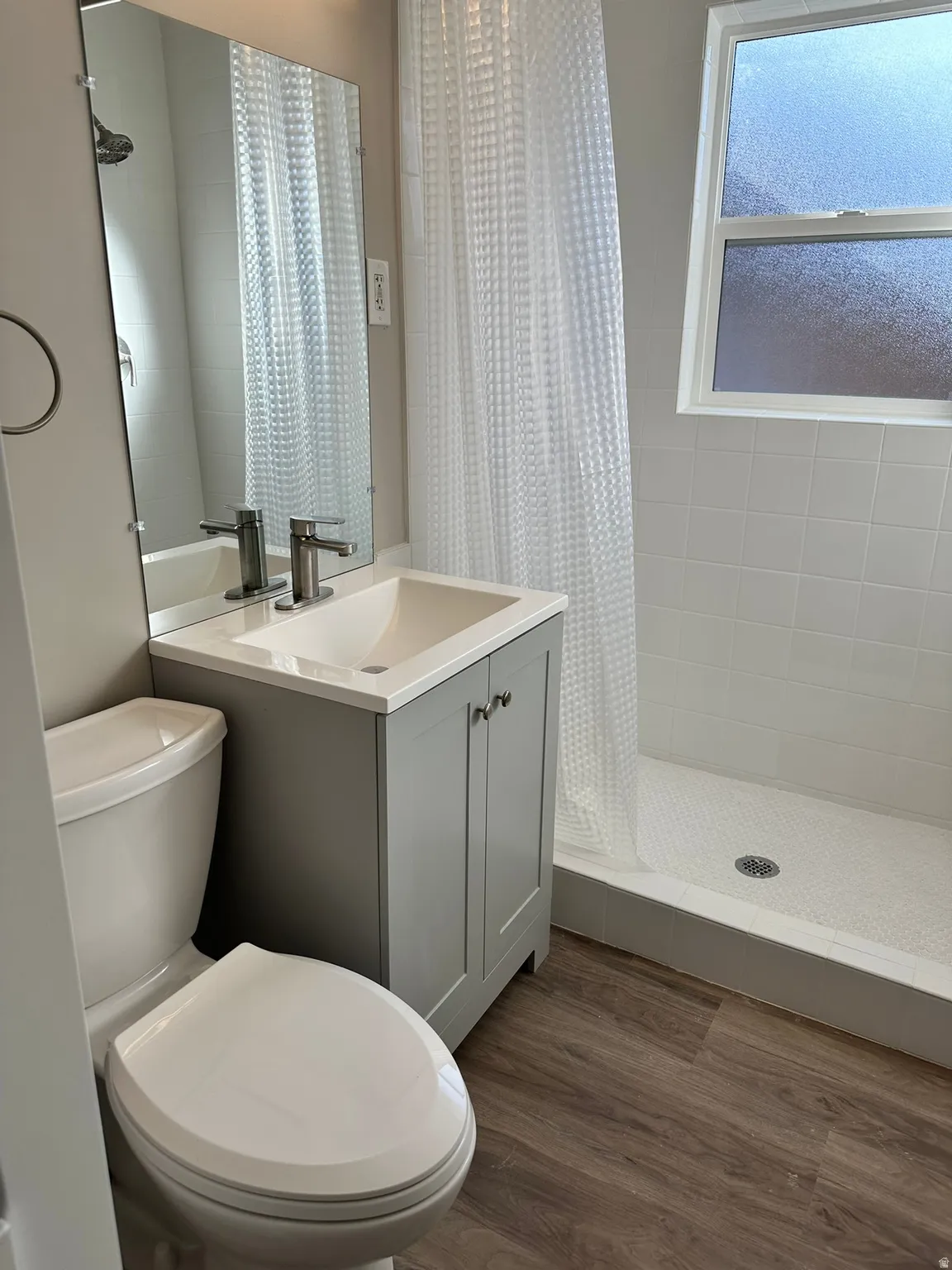 Bathroom featuring a gray vanity with an integrated sink, chrome fixtures, a shower with white subway tile surround, and wood-finish flooring