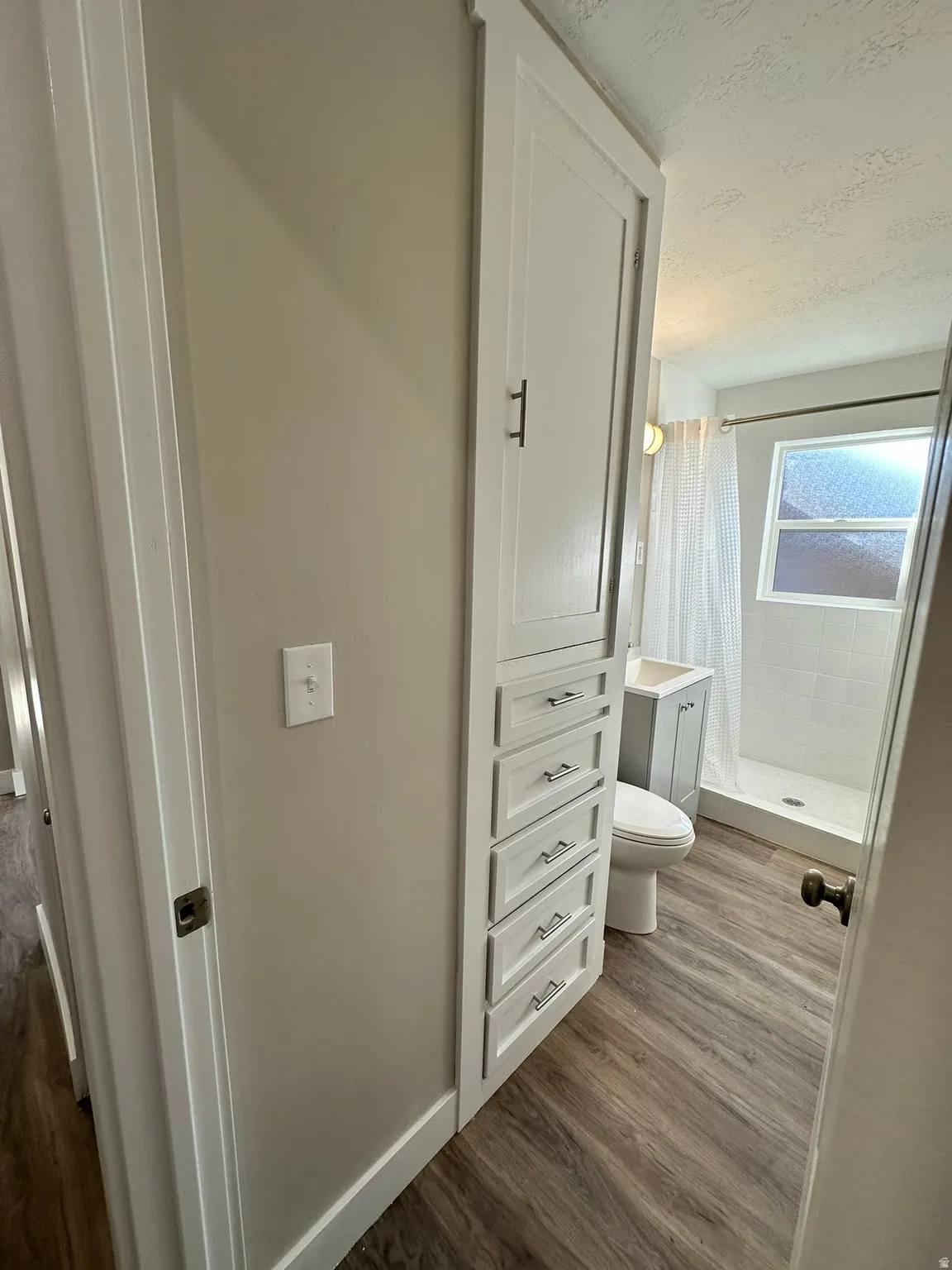 Built-in storage cabinet with multiple drawers, wood-finish flooring, a white vanity with a rectangular sink, and a shower stall with a white tile surround