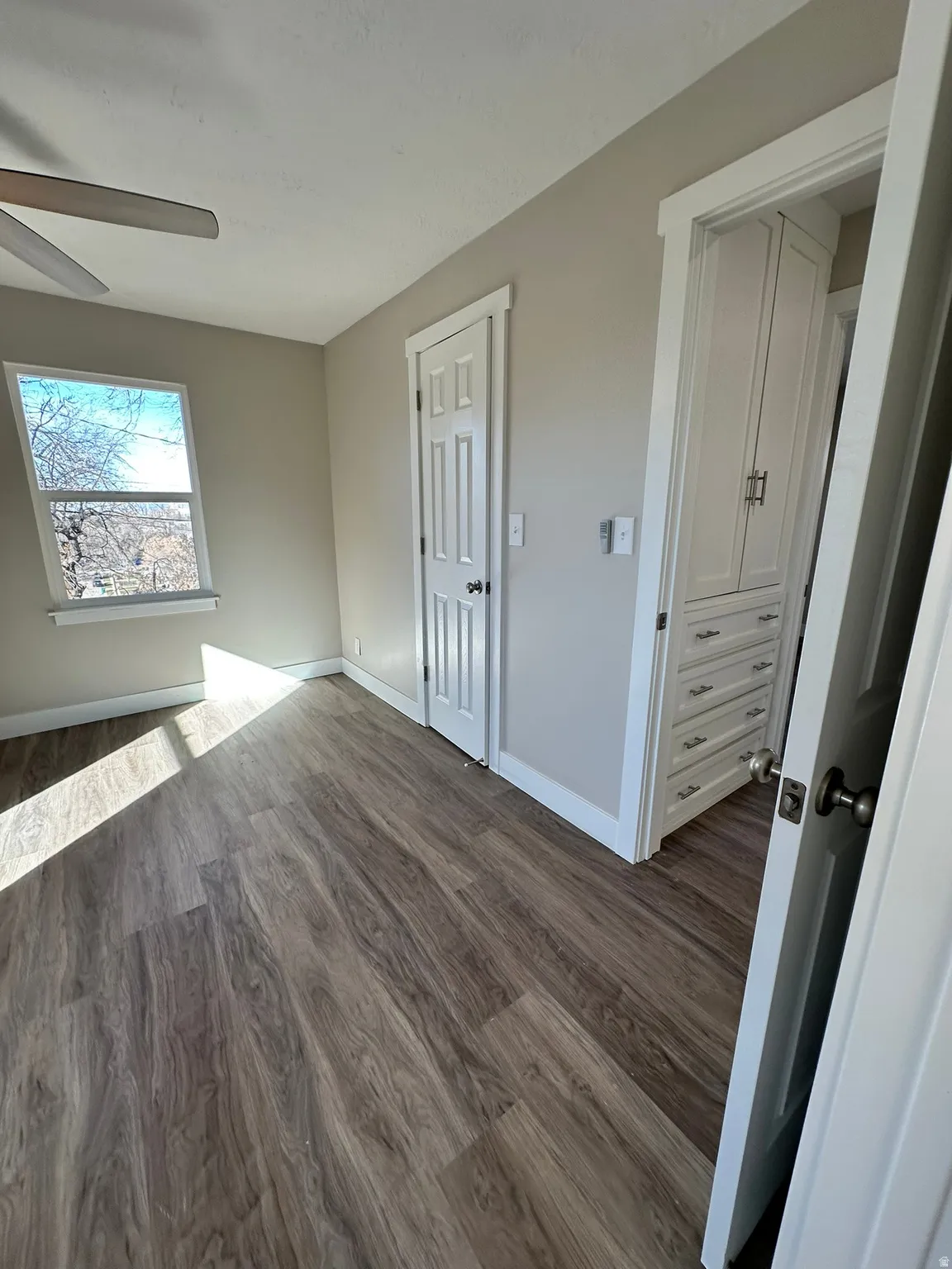 Wood-finish flooring with a window, white trim, and a built-in cabinet with drawers and hardware