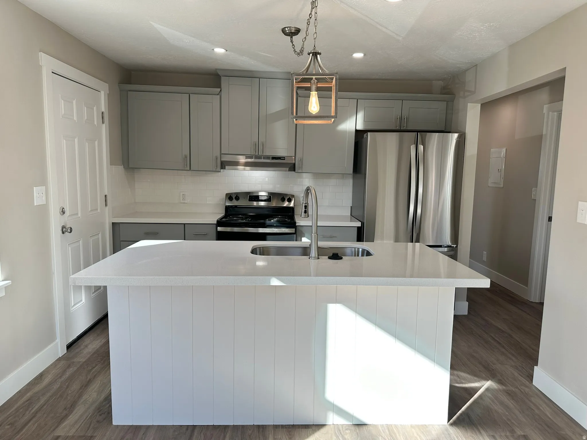 Kitchen featuring a center island with sink, stainless steel appliances, light gray cabinetry, and wood-finish flooring