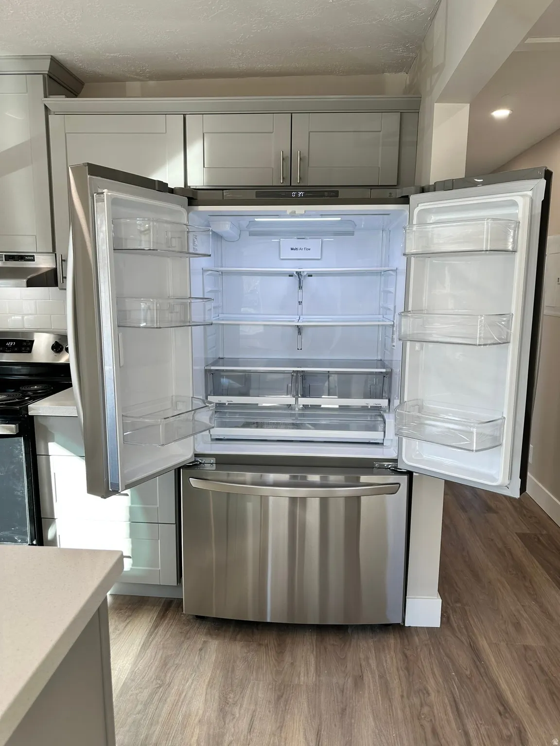 Stainless steel French door refrigerator, light gray shaker cabinetry, subway tile backsplash, and wood-finish flooring