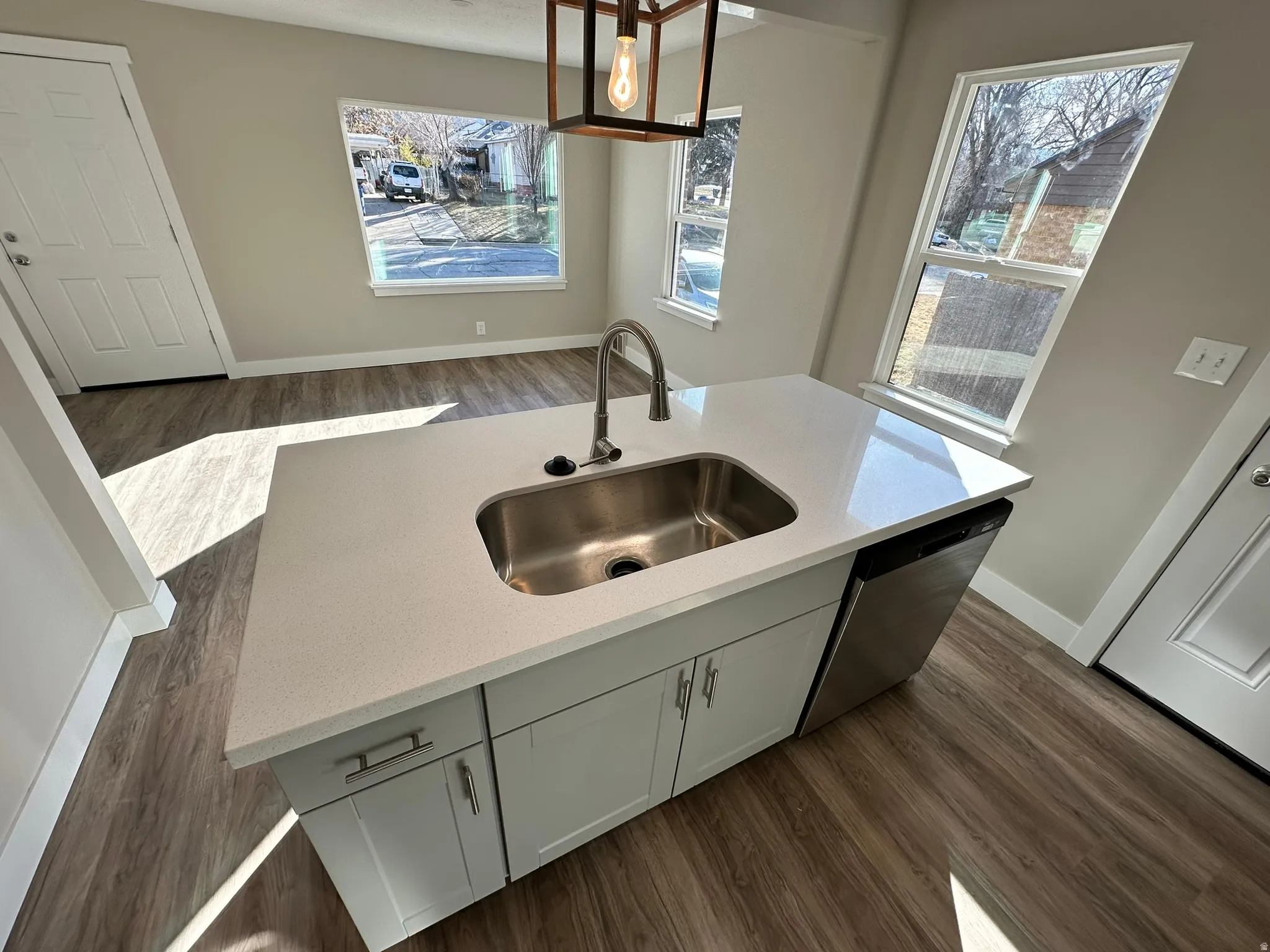 Kitchen island with a stainless steel sink, light-toned countertop, light gray cabinetry, and wood-finish flooring