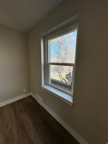 Wood-finish flooring with white trim, a double-hung window, and neutral wall paint