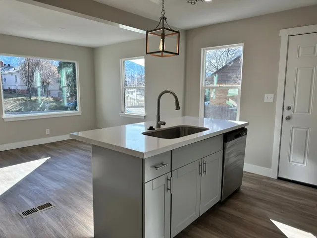 Kitchen island with a light-toned countertop, integrated sink, and stainless steel dishwasher