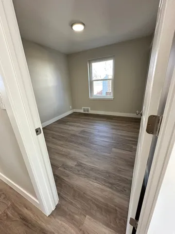 Neutral tone wall paint, wood-finish flooring, single window, and a ceiling-mounted light fixture