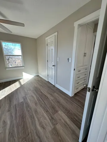 Wood-finish flooring with a window, white trim, and a built-in cabinet with drawers and hardware