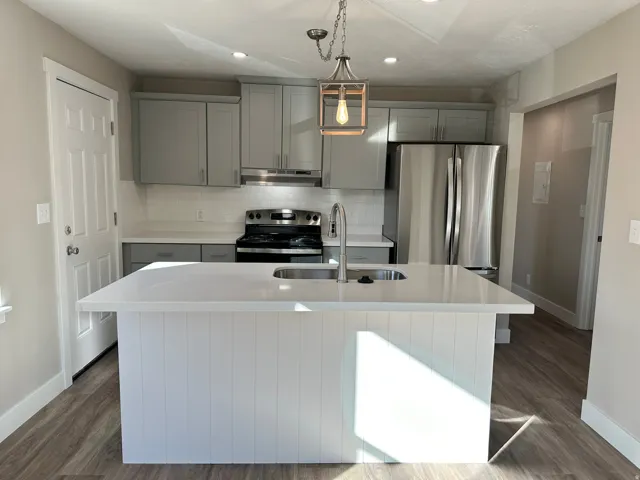Kitchen featuring a center island with sink, stainless steel appliances, light gray cabinetry, and wood-finish flooring