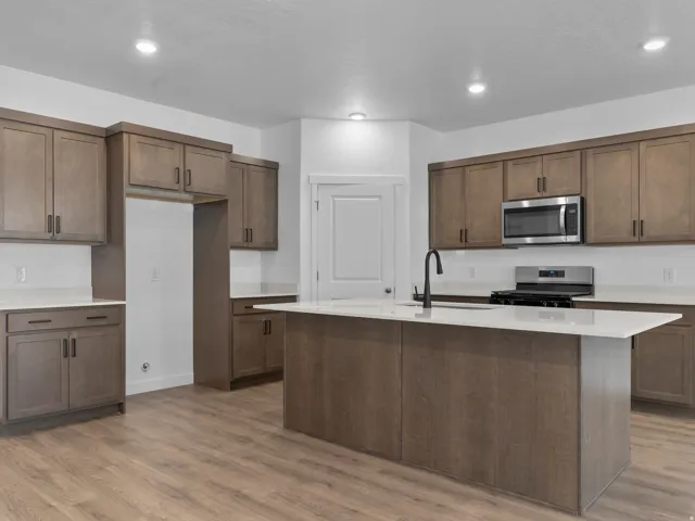 Wood-finish flooring, ample cabinetry with dark hardware, a central island with a white countertop, recessed lighting, and a stainless steel appliance package