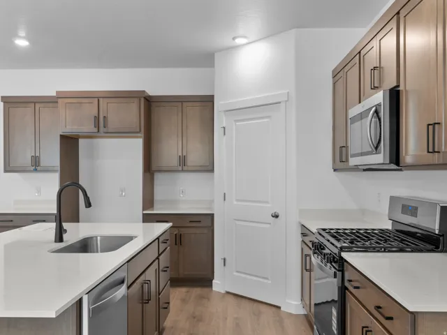 Wood-finish flooring, white countertops, built-in stainless steel microwave, gas range, and a stainless steel sink with a black gooseneck faucet