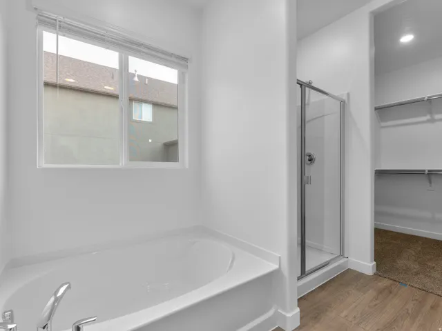 Soaking tub with chrome fixtures, glass-enclosed shower, wood-finish flooring, and a walk-in closet with built-in shelving