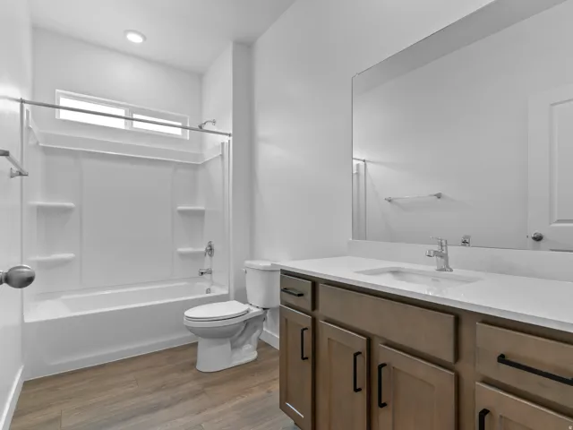 Wood-finish flooring, a contemporary vanity with a white countertop and integrated sink, a white toilet, and a bathtub with an overhead window