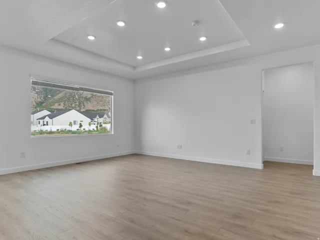 Recessed lighting, tray ceiling, large picture window, wood-finish flooring, and crisp white walls