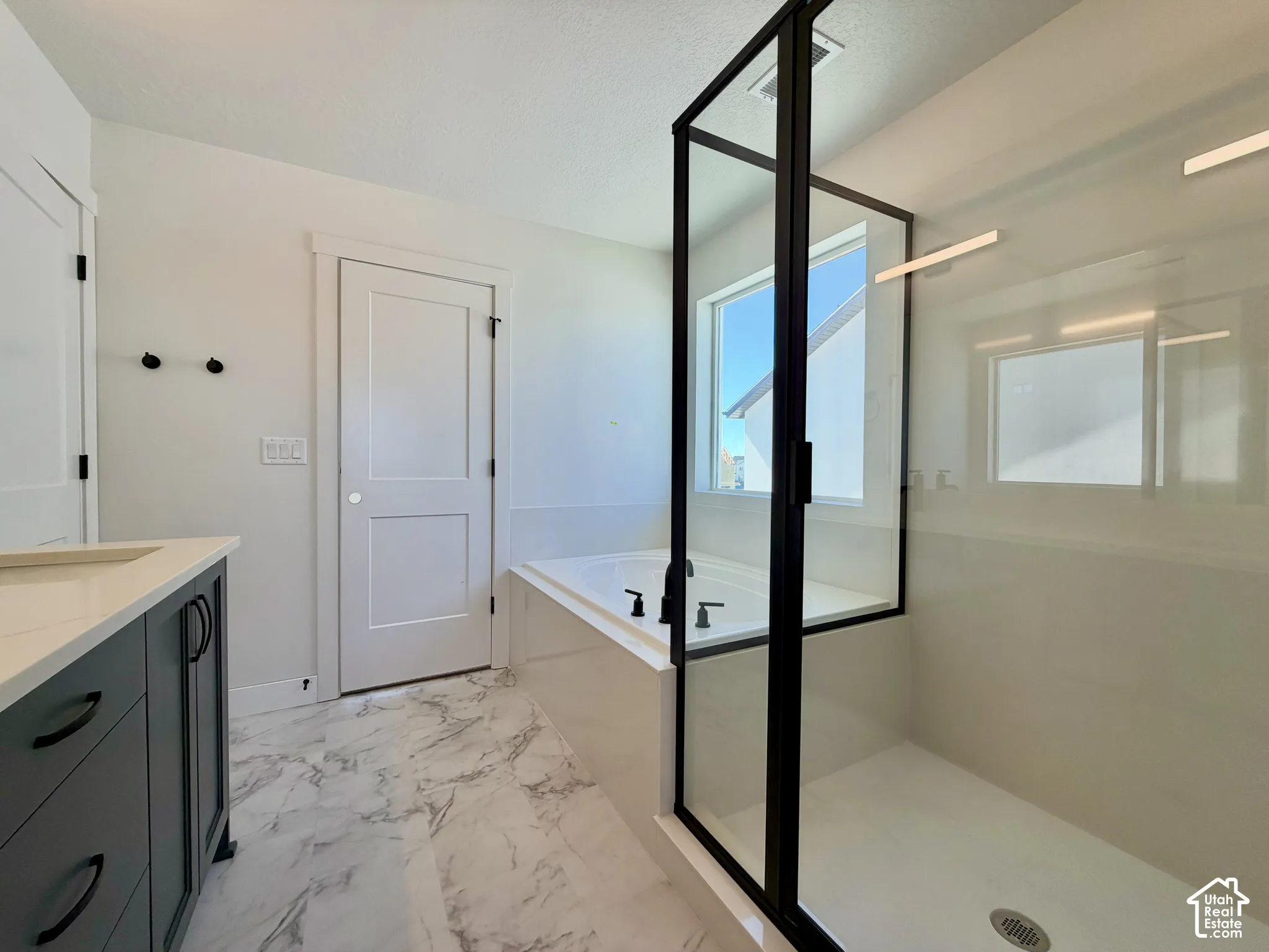 Freestanding soaking tub, glass-enclosed shower, dark-finish vanity with countertop, and large format floor tile