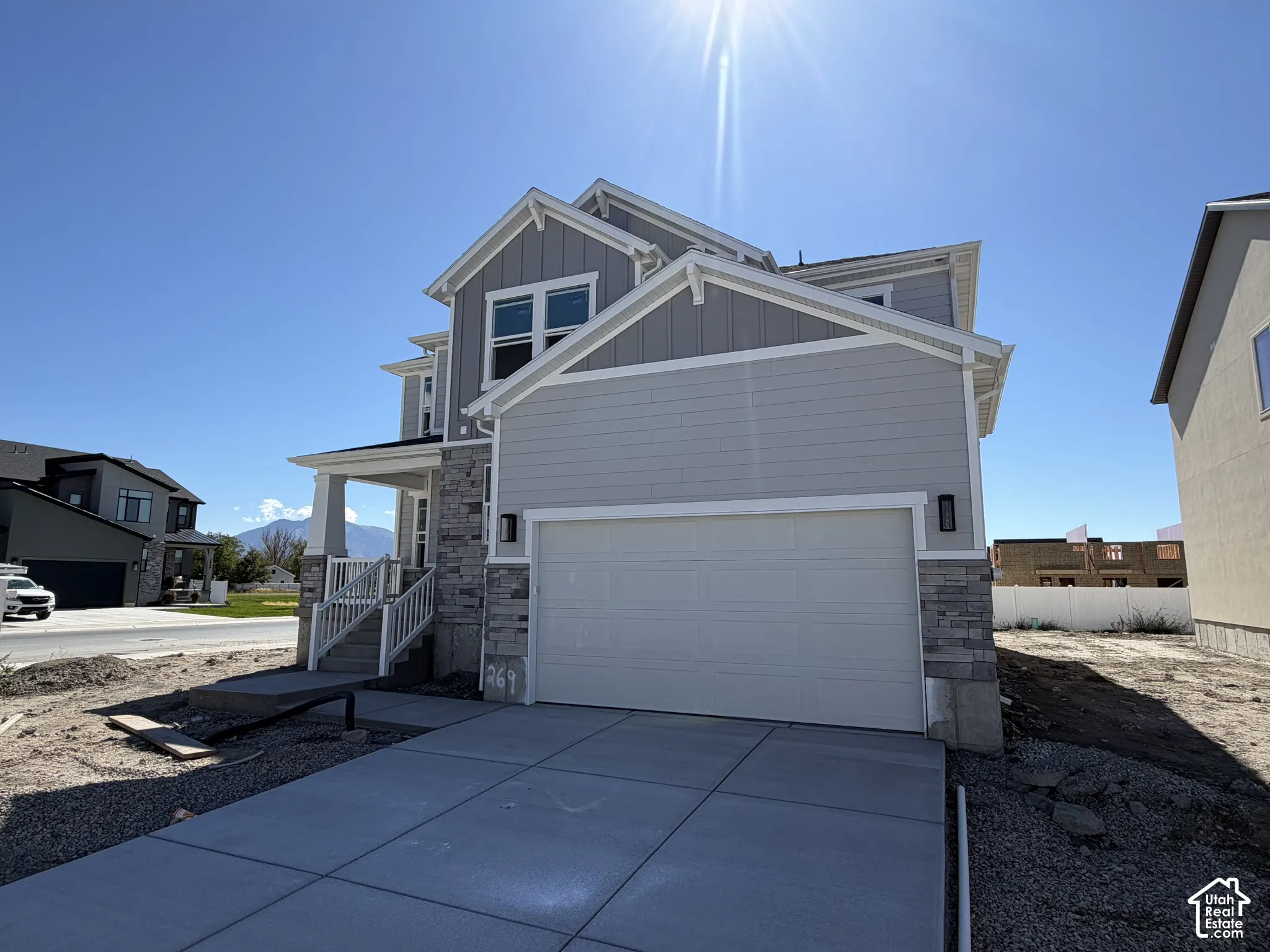 Contemporary two-story residence featuring light gray siding and vertical paneling, stone accents, a covered porch with white railings, and an attached garage with a concrete driveway