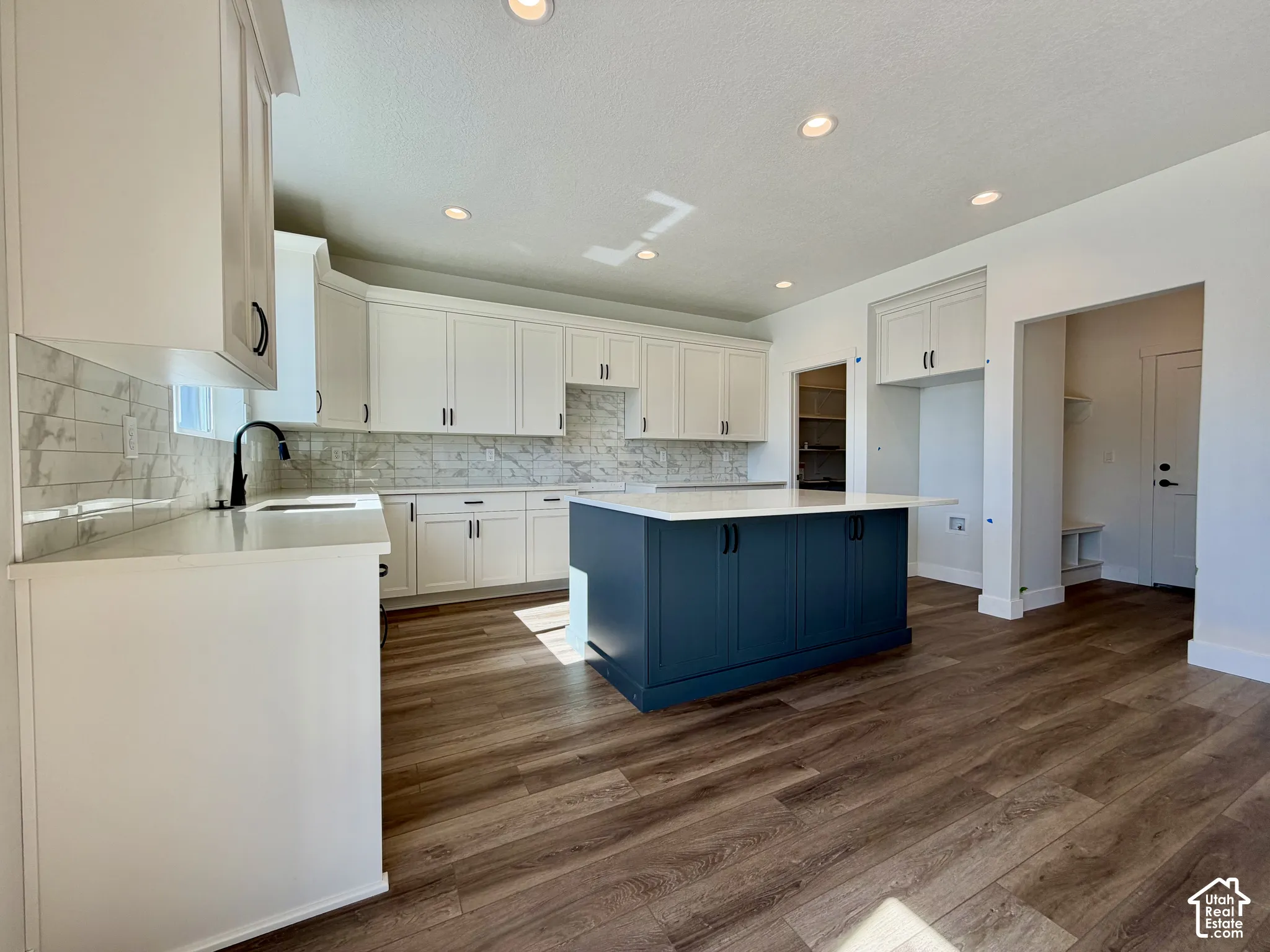 Kitchen featuring white cabinetry, a blue island with a light-toned countertop, wood-finish flooring, and a marble-patterned backsplash