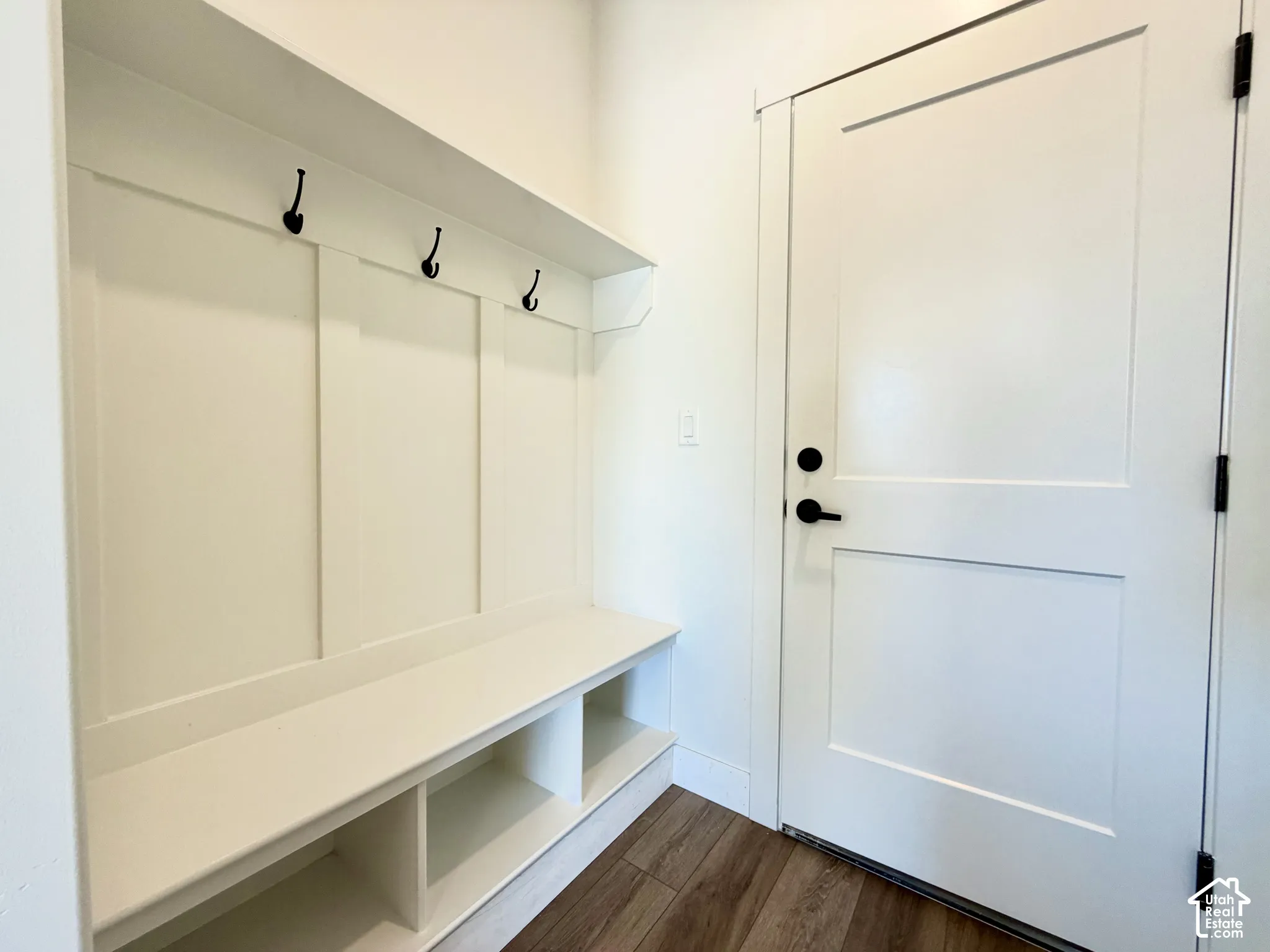Built-in mudroom bench with cubby storage, three black coat hooks, and wall paneling
