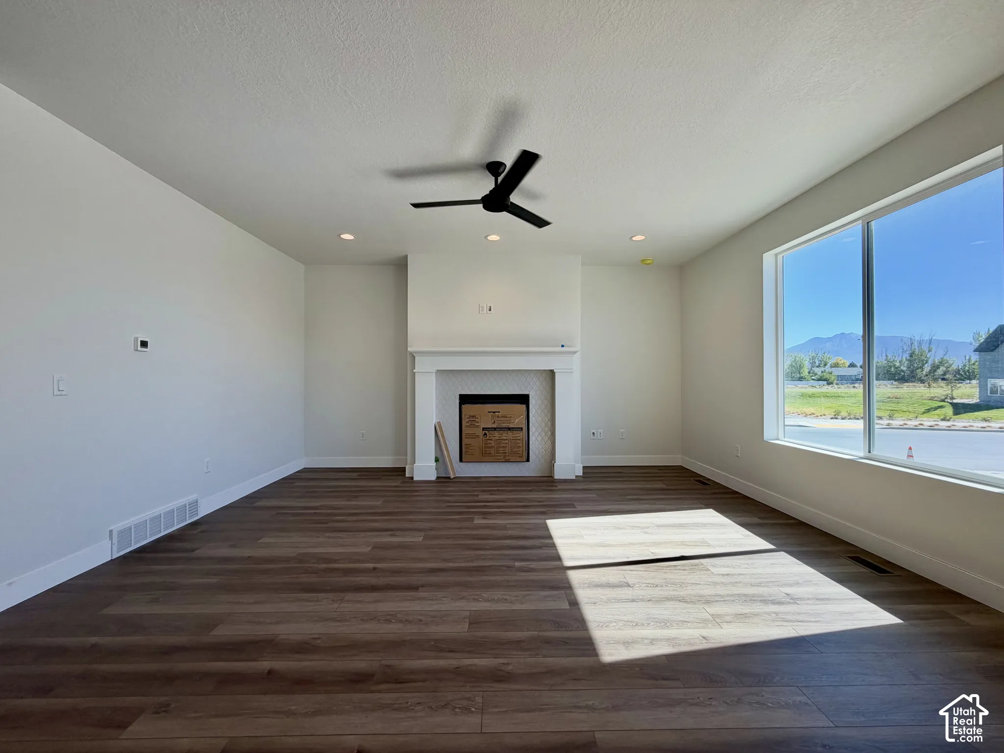 Spacious room featuring wood-finish flooring, a built-in fireplace with a white mantel, and a ceiling fan