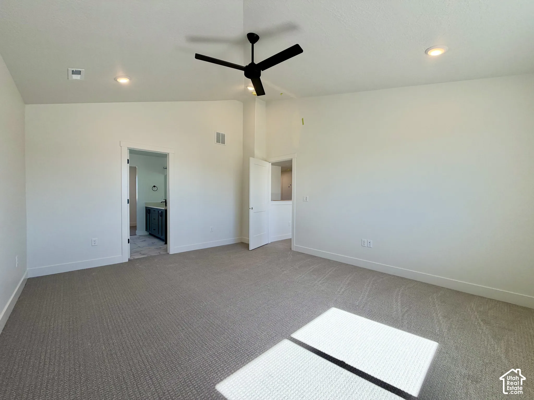 Spacious interior featuring neutral carpet, recessed lighting, a modern ceiling fan, and access to an ensuite bathroom with a dark wood-finish vanity