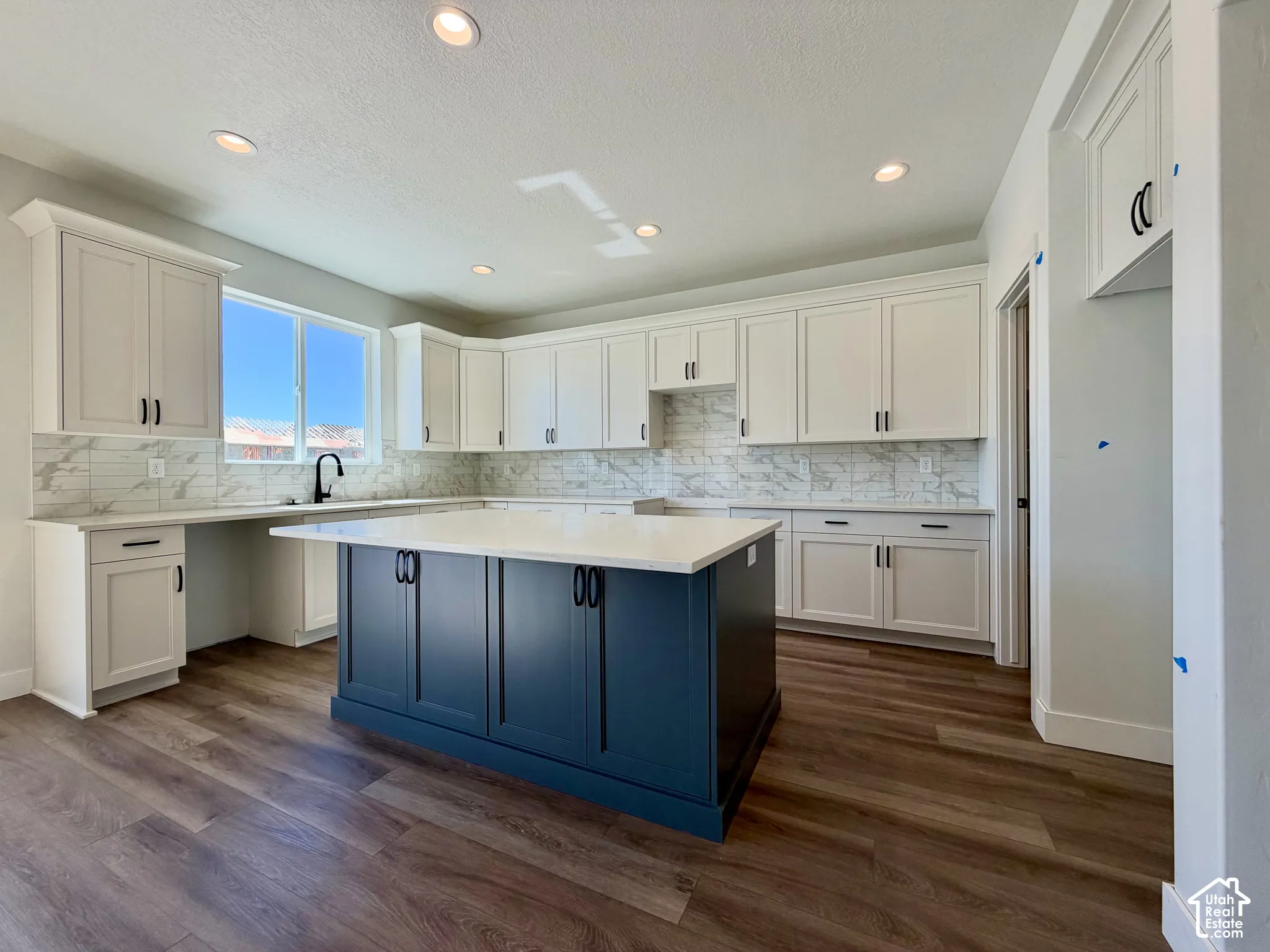 Gourmet kitchen featuring white shaker cabinetry, an expansive central island with dark cabinetry, stone countertops, a full-height tile backsplash, and wood-finish flooring