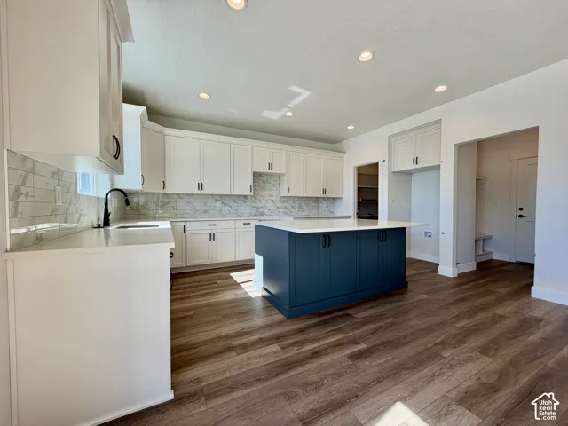 Kitchen featuring white cabinetry, a blue island with a light-toned countertop, wood-finish flooring, and a marble-patterned backsplash