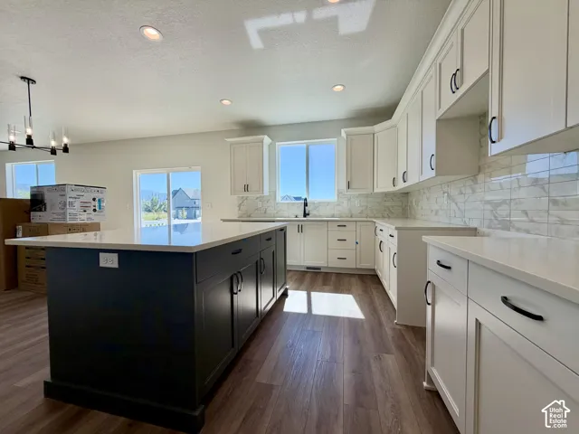 Modern kitchen featuring white shaker cabinetry, an expansive dark-toned island, light-toned countertops, and wood-finish flooring