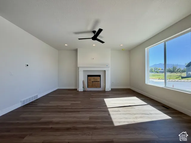 Spacious room featuring wood-finish flooring, a built-in fireplace with a white mantel, and a ceiling fan