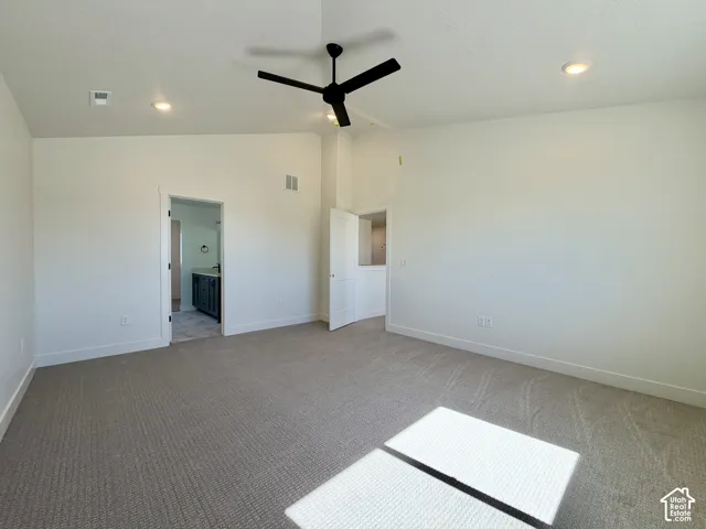 Spacious interior featuring neutral carpet, recessed lighting, a modern ceiling fan, and access to an ensuite bathroom with a dark wood-finish vanity