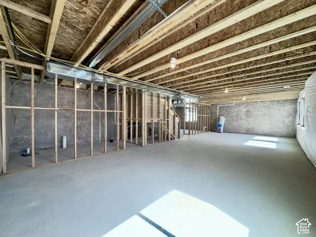 Unfinished basement with concrete flooring, exposed wooden ceiling joists, and framed partition walls